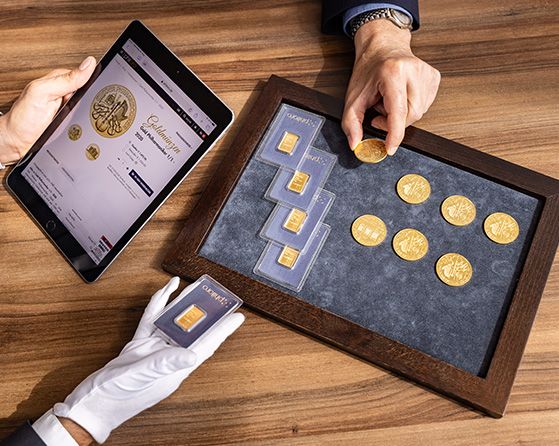 Eine Person präsentiert einer anderen Goldmünzen und -barren auf einem Tablett.