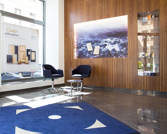 Ein Foto des Wartebereichs der Filiale in Graz. Er enthält 2 Stühle und einen Tisch für die Wartezeit und hat an der Wand eine Vitrine mit philoro Produkten.