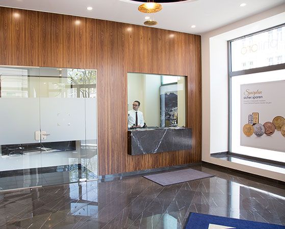 Der Empfangsbereich der philoro Filiale in Graz. Die Wand wird verziert durch eine hölzerne Wandvertäfelung. Das Empfangspult ist aus einem edlen Stein. Ein Mitarbeiter steht hinter dem Pult, um Kunden zu begrüßen.