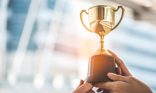 Ein goldener Pokal wird in die Höhe gehalten.