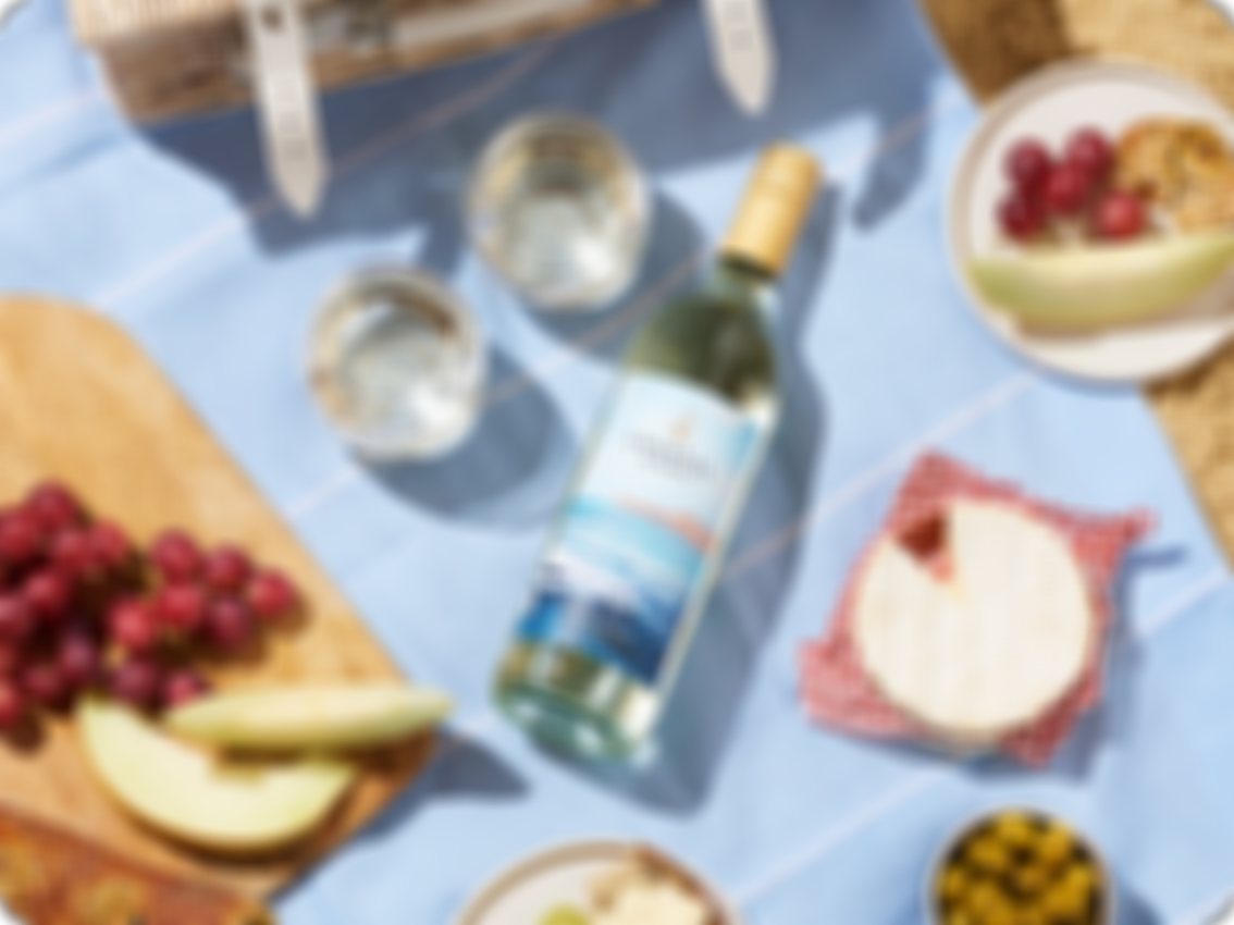 coastal reserve picnic on the beach, wine bottle on a towel next to brie cheese and fruit, CR PGrigio Beach Picnic 4x5 EUR 2