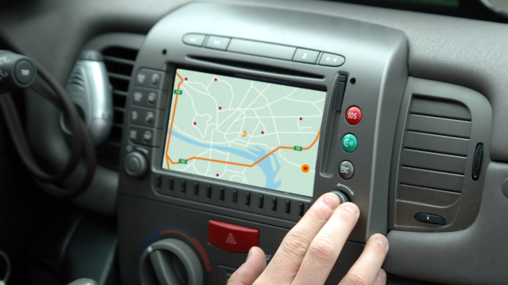 Salpicadero de un coche con el mapa del GPS en la pantalla central y una mano ajustando un mando, utilizado para ilustrar la planificación y el control de las horas de conducción