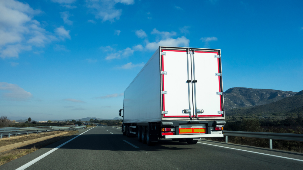 Camión blanco de gran tonelaje circulando por una autopista entre zonas rurales, imagen relacionada con optimizar rutas de transporte.