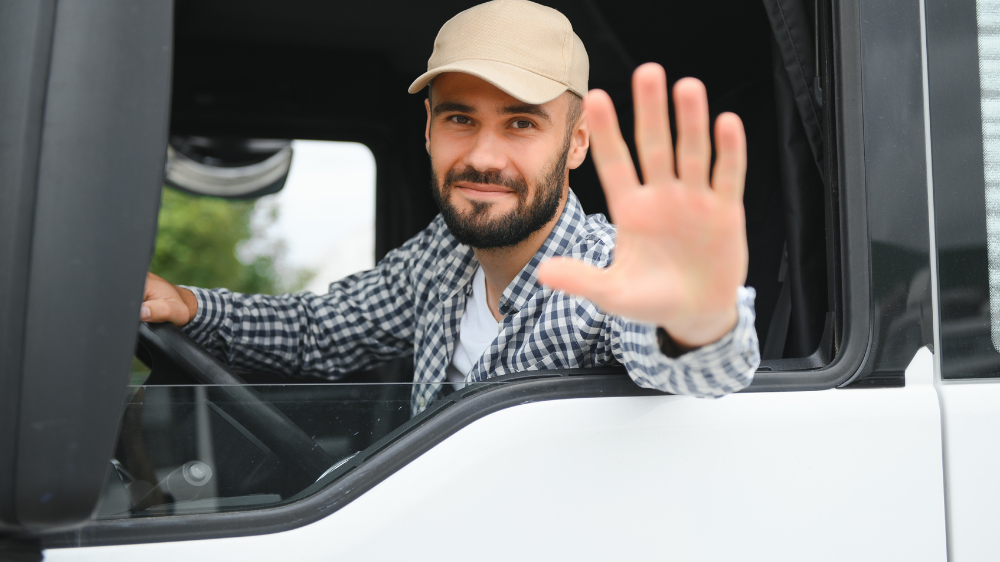 Chauffeur souriant dans un camion, saluant par la fenêtre ouverte, illustrant la traçabilité transport lors de l’exécution des tournées de livraison