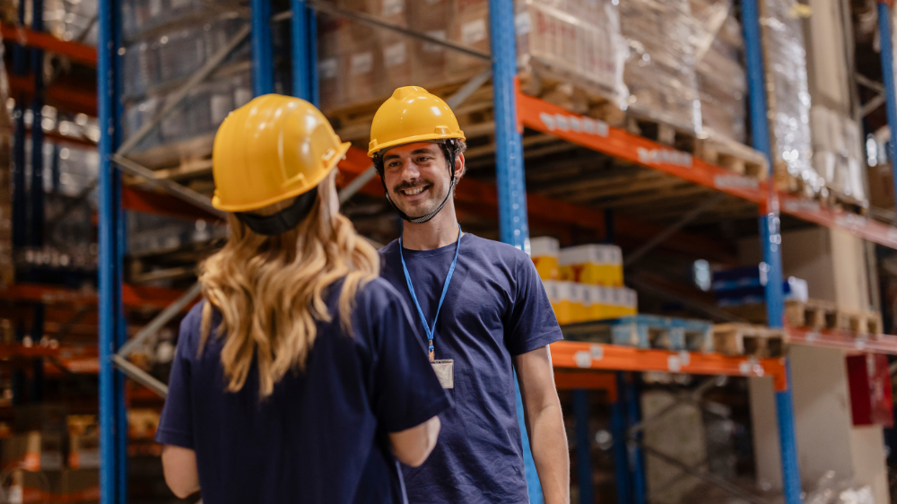 Deux opérateurs logistiques portant des casques jaunes discutent dans un entrepôt, coordination et visibilité transport en temps réel avec RTTV TMS.