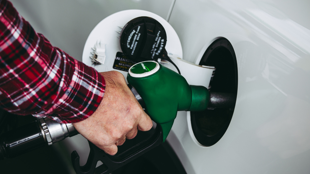 Personne en chemise à carreaux rouges faisant le plein d’un véhicule blanc avec un pistolet vert — image illustrant le prix des biocarburants et leur usage au quotidien.