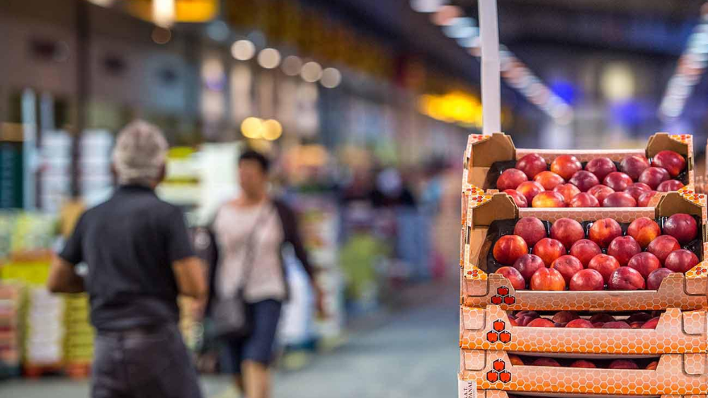 Caisses de pommes rouges sur un étal de MIN marché, avec des acheteurs flous en arrière-plan.
