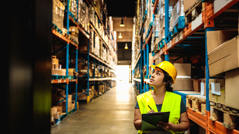 Opérateur en gilet haute visibilité et casque inspectant des rayonnages dans un entrepôt spacieux avec un clipboard dans un flux piloté par un warehouse management software