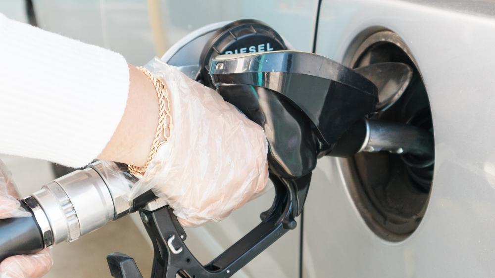 Gros plan sur une personne faisant le plein de gazole, tenant le pistolet de pompe avec une main gantée, manche blanche et bracelet doré visibles, illustrant concrètement l’impact de l’indice CNR gazole sur le coût du carburant.