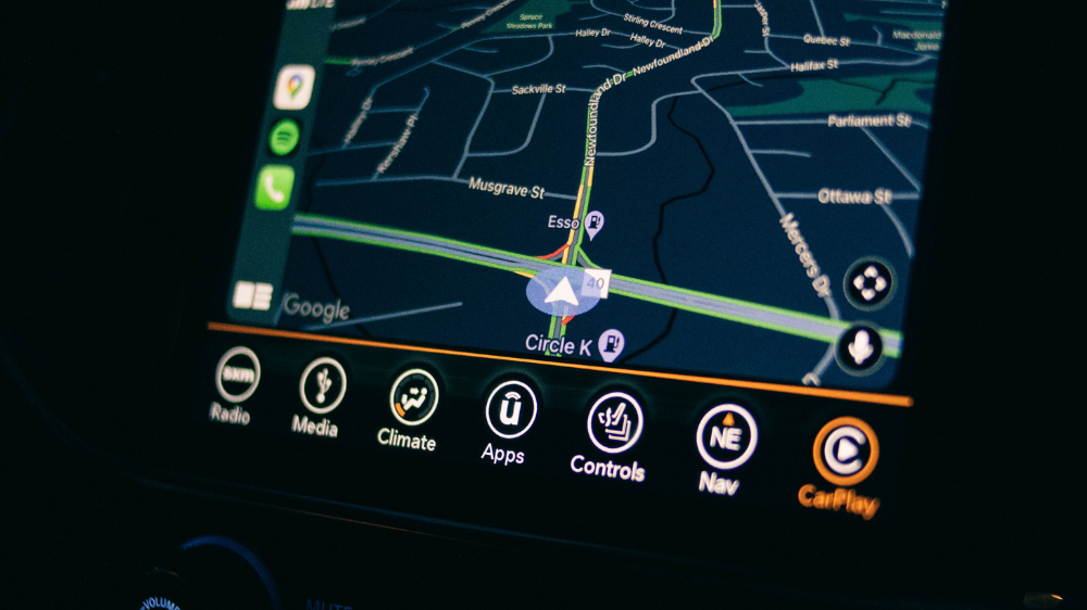 Primer plano de la pantalla del sistema de navegación de un coche que muestra un mapa con rutas destacadas e iconos de control, utilizada junto a un rastreador GPS para visualizar la posición en tiempo real.