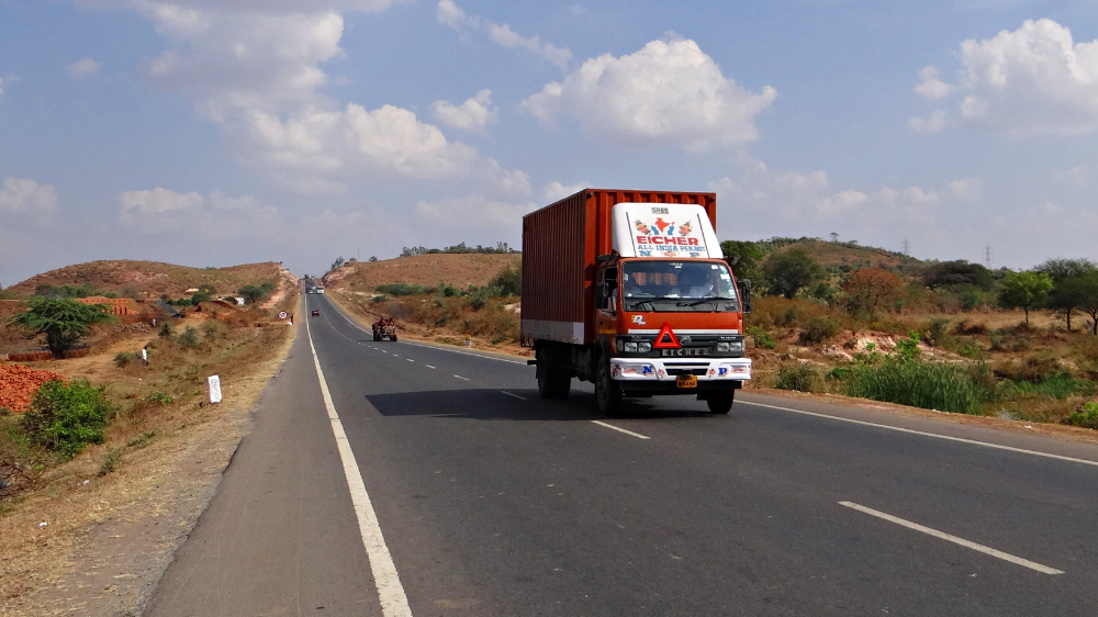 Camión circulando por una autopista larga y desierta en un paisaje rural bajo un cielo parcialmente nublado, cuya trayectoria puede seguirse con un rastreador GPS.