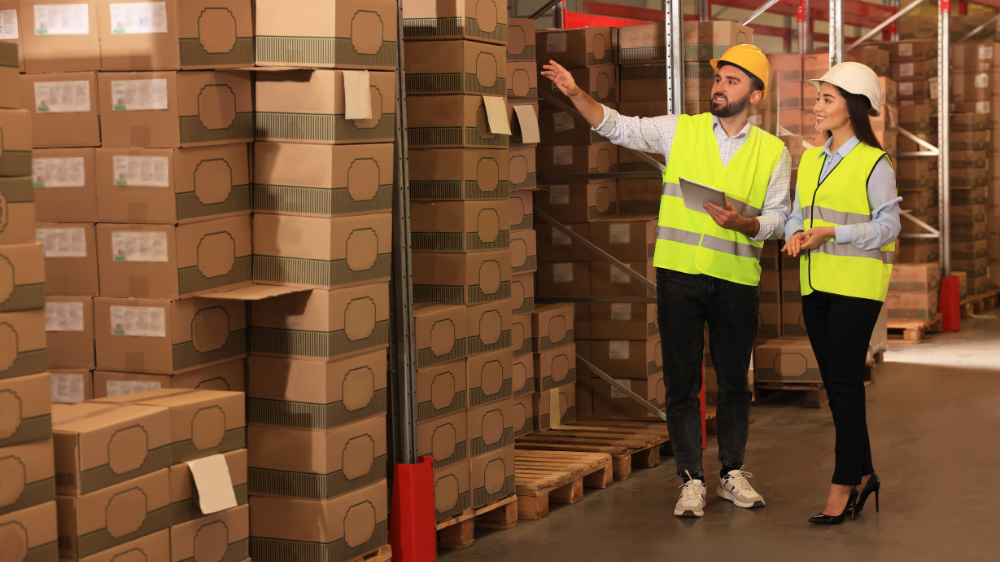 Travailleurs d’entrepôt vérifiant le stock minimum, entourés de cartons empilés sur des étagères.