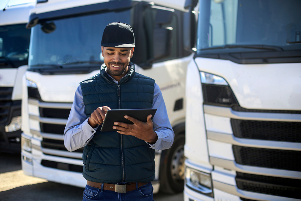 Gestionnaire de flotte souriant avec tablette devant ses camions piloté par un ERP transport