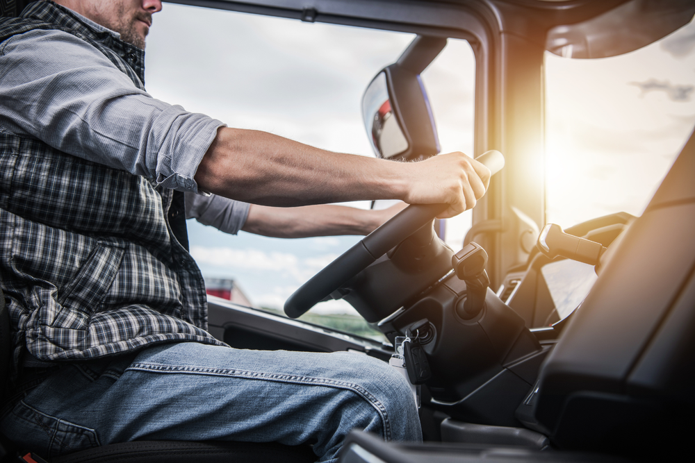 Conducteur en gilet à carreaux au volant d’un camion, en mission de cabotage routier sous le soleil.