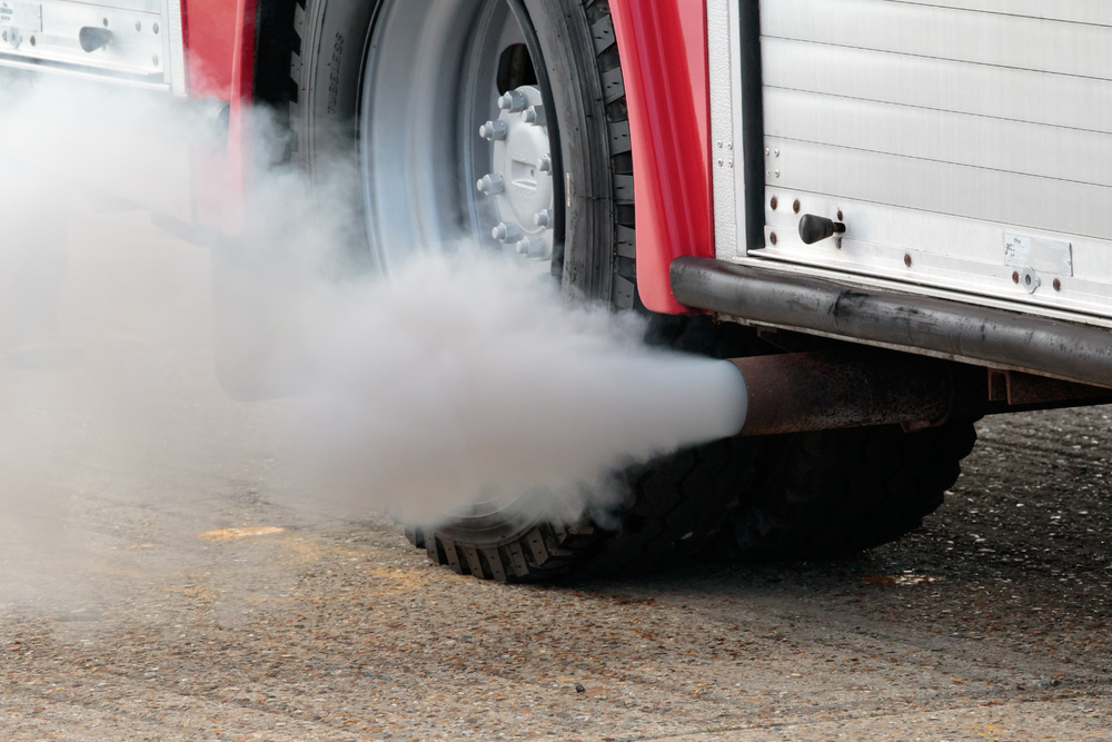 Pot d’échappement d’un véhicule émettant une fumée blanche épaisse, sur fond de béton, illustrant les enjeux de pollution liés au transport.          Demander à ChatGPT