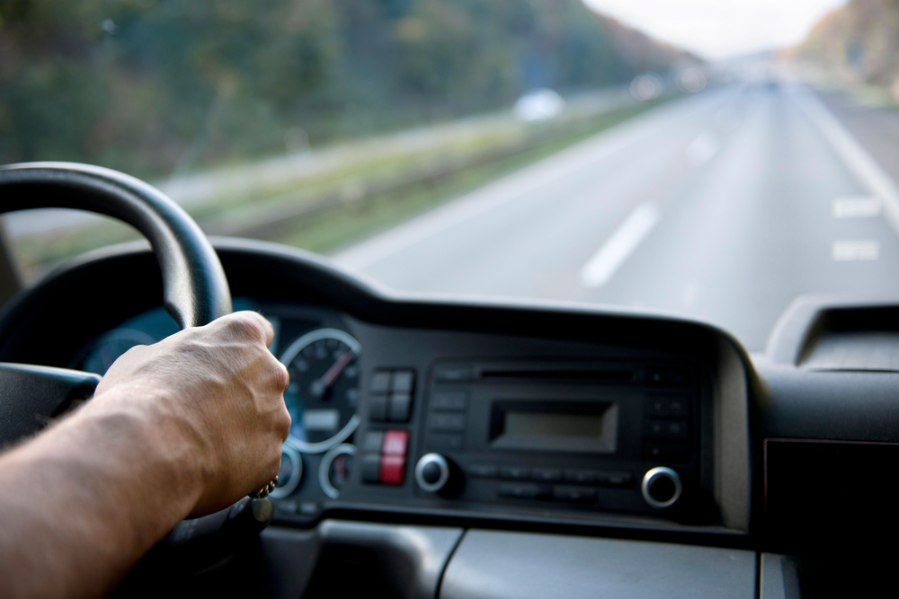 Conducteur tenant le volant d’un camion de groupage sur l’autoroute, avec le tableau de bord visible et le paysage flou en arrière-plan.