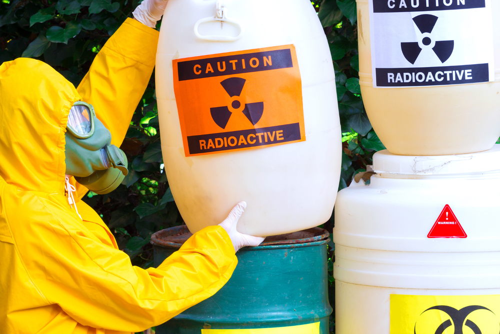 carta de porte ADR – persona con equipo de protección manipulando barriles etiquetados 'Caution Radioactive' en exterior, rodeado de vegetación