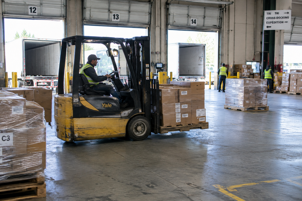 Cariste déplaçant des palettes de marchandises sur une plateforme de tri lors d'une opération de messagerie routière.