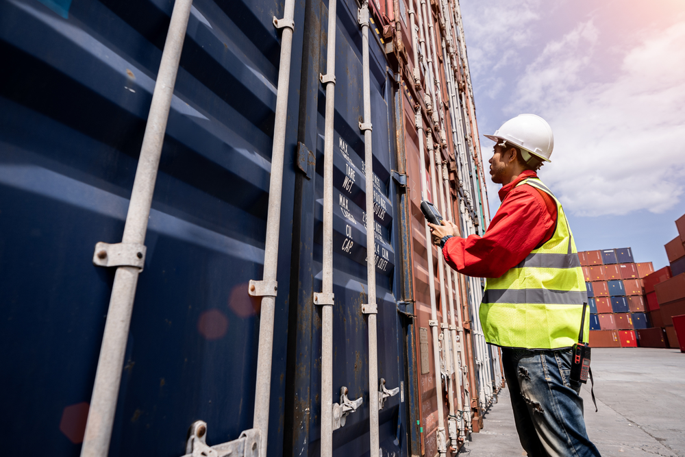 Travailleur logistique vérifiant des conteneurs de fret international dans un port dédié à l’import export