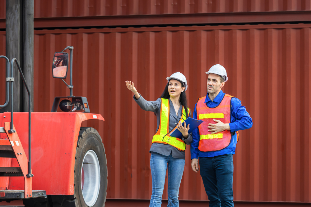 Supervisores de transporte revisando KPIs de transporte con checklist en zona de contenedores logísticos