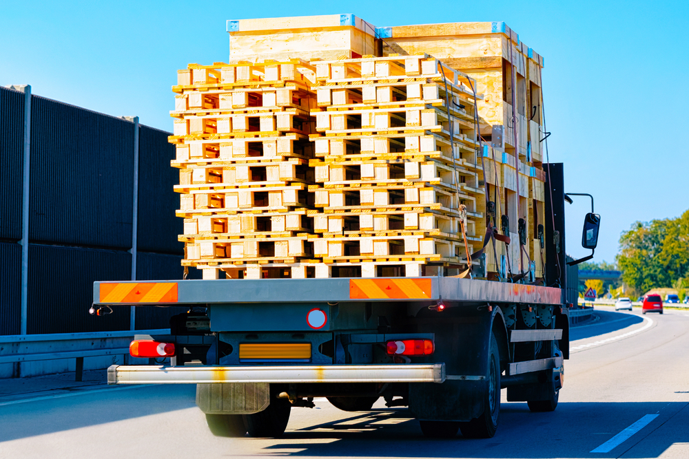 Camión transportando pallets de madera apilados por la autopista bajo un cielo azul despejado.