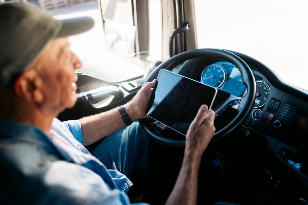 Chauffeur de poids lourd utilisant une tablette pour suivre son remboursement TICPE depuis sa cabine, concentré sur l'écran avec le volant et le tableau de bord visibles en arrière-plan.