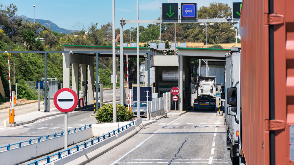 Camions et voitures à un péage autoroutier, avec panneaux de direction de voie et un panneau stop visible.