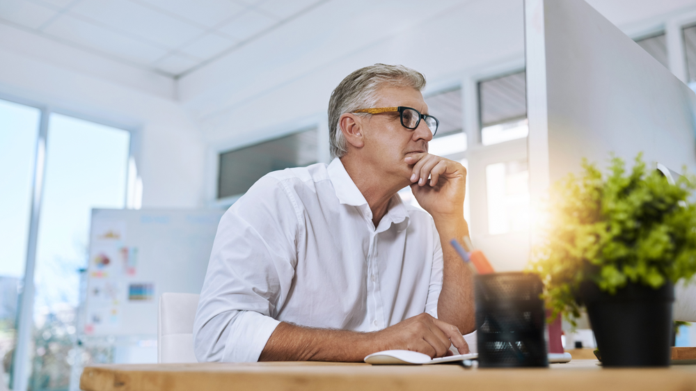 gestion de flotte poids lourds un homme avec lunettes dans un bureau lumineux assis à un bureau devant un ordinateur expression pensive avec une plante au premier plan