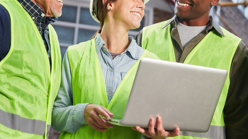 Tres trabajadores de obra con chalecos revisan el documento de transporte en un portátil
