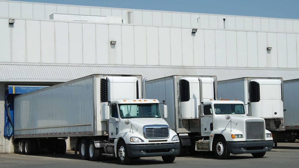 Dos camiones blancos estacionados en un muelle de carga de un almacén industrial, simbolizando la logística de distribución.