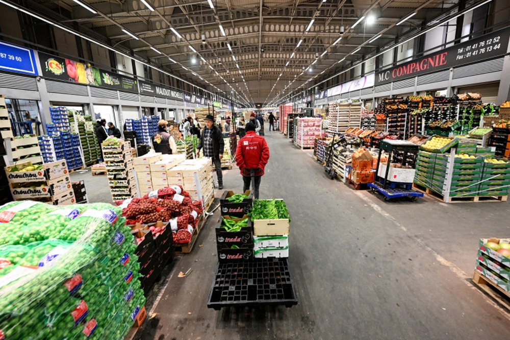 Personne marchant dans les allées d’un MIN marché intérieur, entre des piles de fruits et légumes sous un éclairage intense.