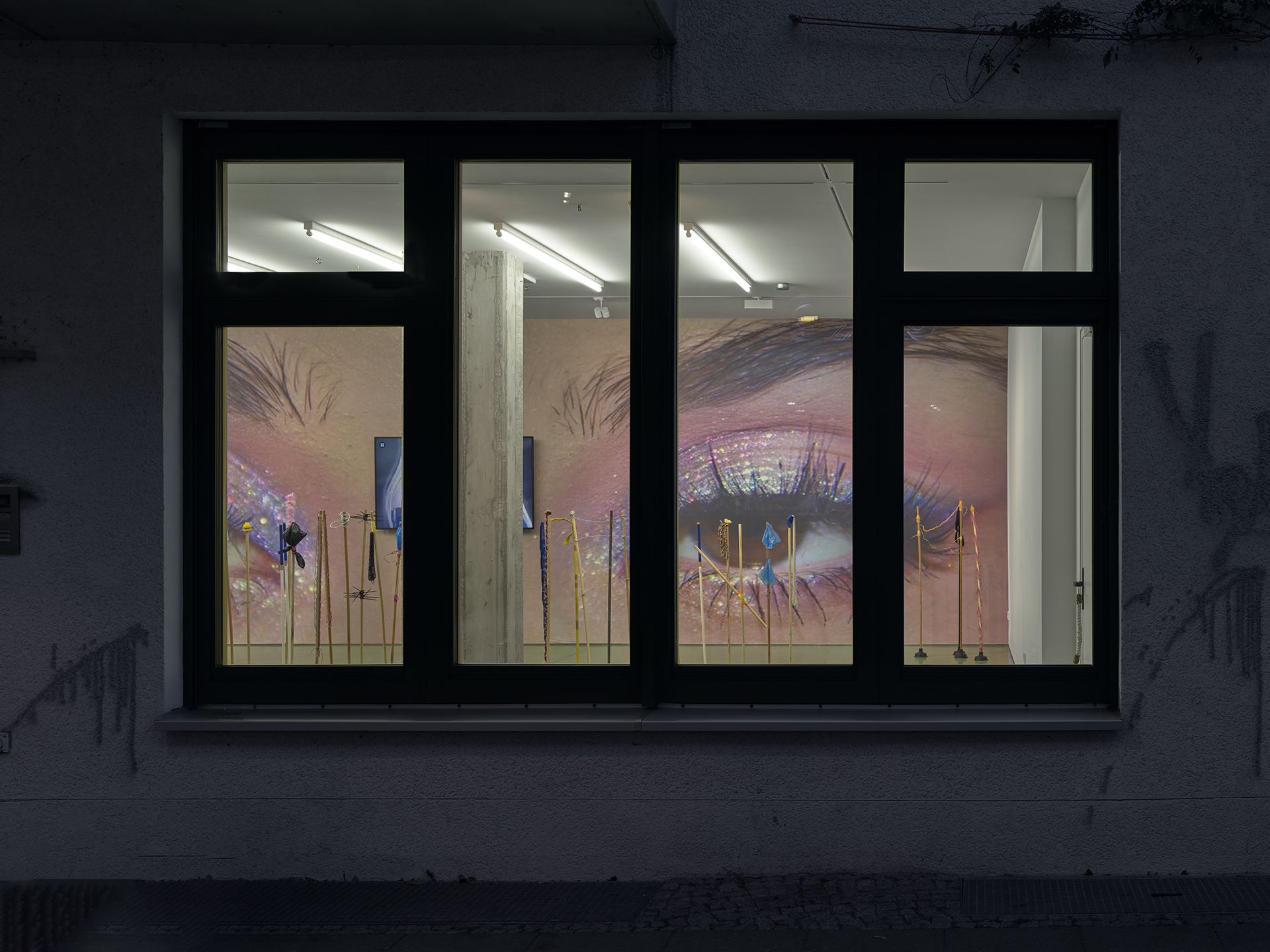 Storefront window displaying large, colorful images of eyes with glittery makeup, visible through three glass panes at night.