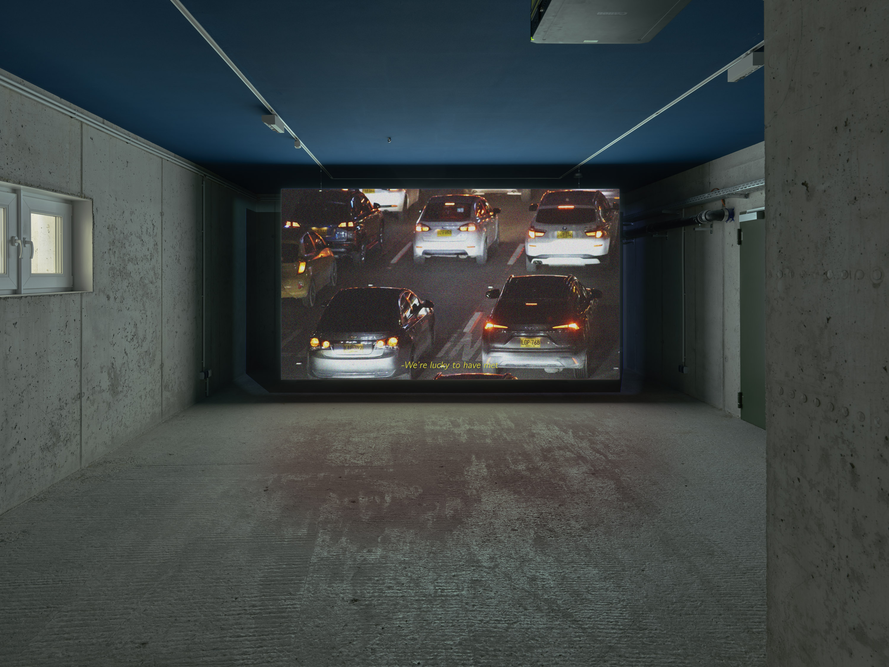 A dimly lit room with a large screen showing a traffic scene at night, featuring several cars with illuminated taillights.