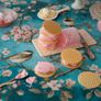 Waffle ice cream sandwiches with pink filling on a floral tablecloth featuring birds and blossoms, surrounded by plates and a spoon.