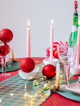 Feestelijk gedekte kersttafel met rood tafelkleed, groene tafellopers, kaarsen, kerstballen, notenkraker en kerstdecoratie.