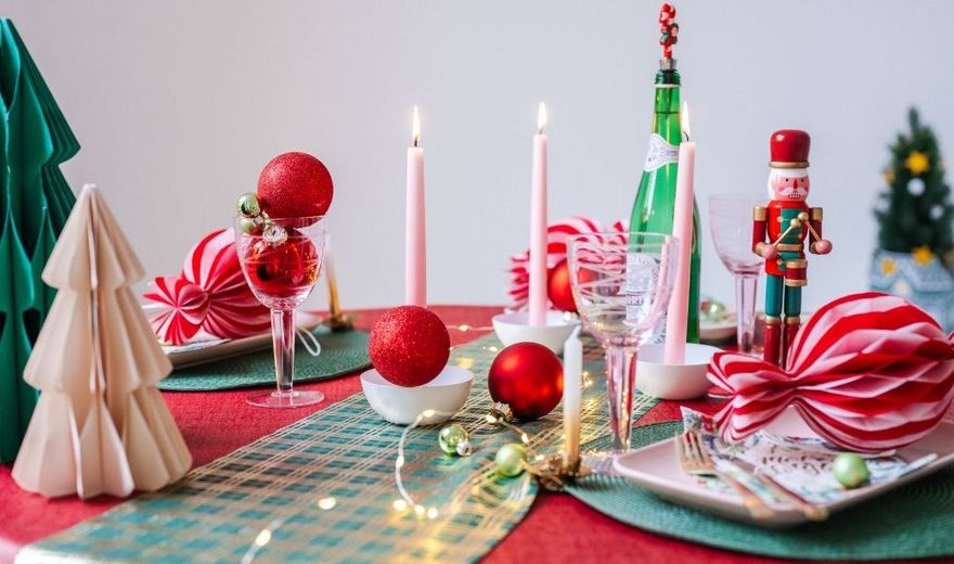 Feestelijk gedekte kersttafel met rood tafelkleed, groene tafellopers, kaarsen, kerstballen, notenkraker en kerstdecoratie.