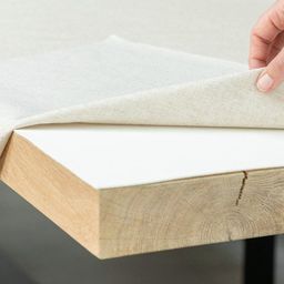 Tafelkleed wordt opgetild en toont een witte tafelmolton op een eiken tafel