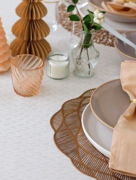Elegant table setting with beige napkins, leaf-shaped napkin rings, glassware, candles, and decorative trees on a textured tablecloth.