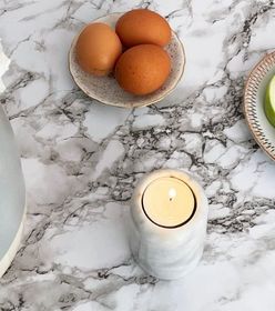 Marble table with a vase of white flowers, a candle, eggs on a plate, sliced green apples, and a decorative plate.