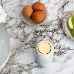 Marble table with a vase of white flowers, a candle, eggs on a plate, sliced green apples, and a decorative plate.