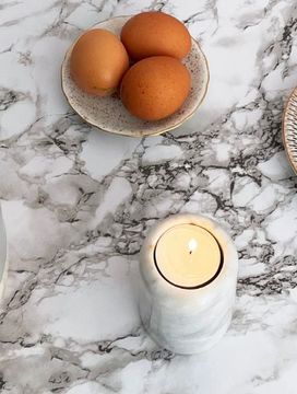 Marble table with a vase of white flowers, a candle, eggs on a plate, sliced green apples, and a decorative plate.
