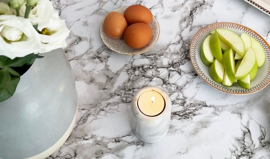 Marble table with a vase of white flowers, a candle, eggs on a plate, sliced green apples, and a decorative plate.