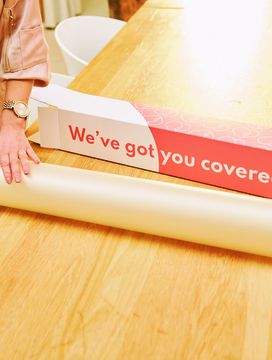Person unrolling white wrapping paper from a red box labeled "We’ve got you covered" on a wooden table.