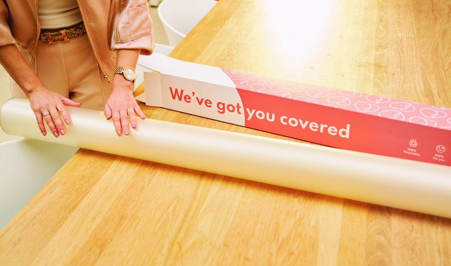 Person unrolling white wrapping paper from a red box labeled "We’ve got you covered" on a wooden table.