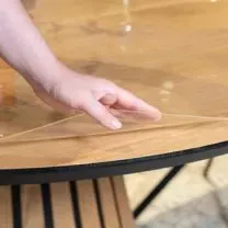 A hand lifting a clear protective film from a wooden table surface.