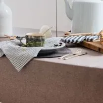A table with a cup of tea, a striped napkin, forks, and a teapot, set in a cozy kitchen atmosphere.