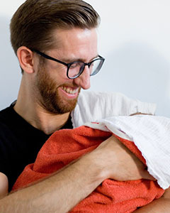 Person hält ein in eine Decke eingewickeltes Baby im Arm.