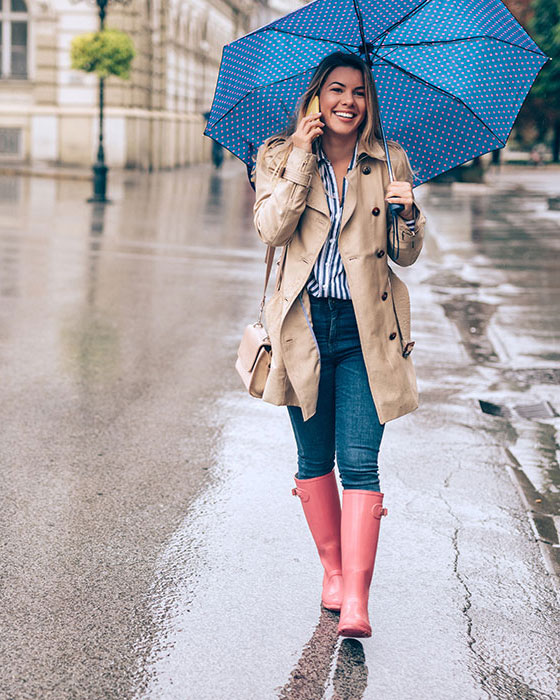 Frau spaziert telefonierend und lächelnd mit einem Regenschirm in der Hand durch den Regen.