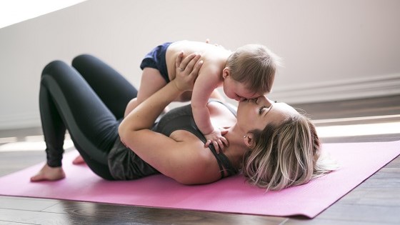 Mutter liegt mit Baby auf einer Trainingsmatte.