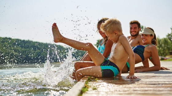 Familie sitzt am Steg und strampelt im Wasser.